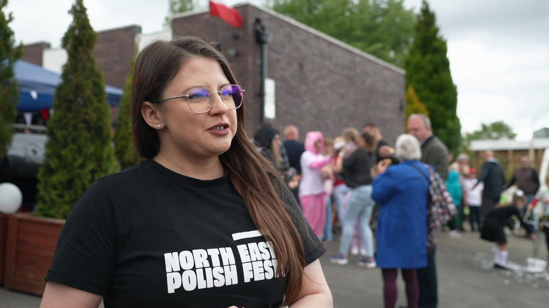 Daria Szymonowicz has brown hair and wears glasses. She is wearing a black T-shirt with white lettering which says "North East Polish Fest"