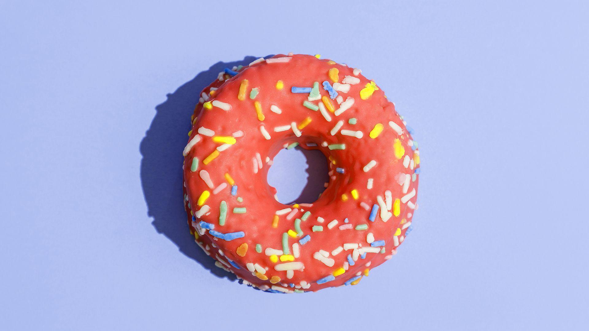 An iced doughnut with sprinkles on a purple background.
