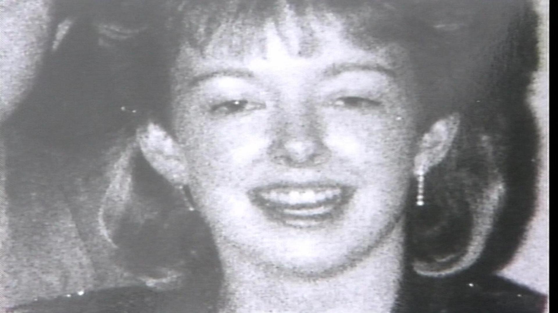 A black and white photograph of Diane Sindall, who has her hair cut into a fringe, smiling at the camera