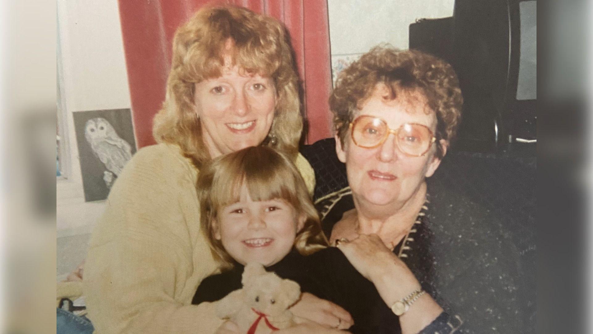 Abi Trotman yn ferch fach yn dal tedi, gyda'i Mam Lindsay Trotman (chwith) a'i Mamgu Sylvia Trounce (dde)