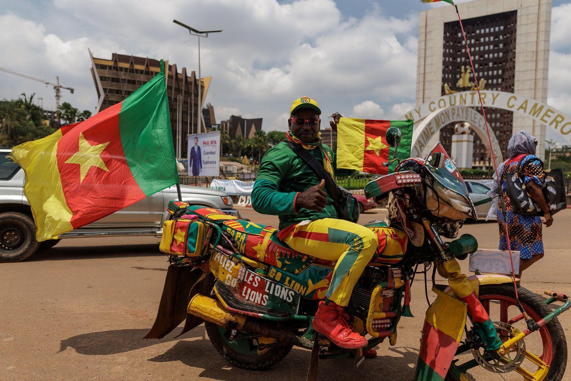 A man poses for photos on his motorbike. The vehicle and his clothes match the yellow, red and green flag he carries.