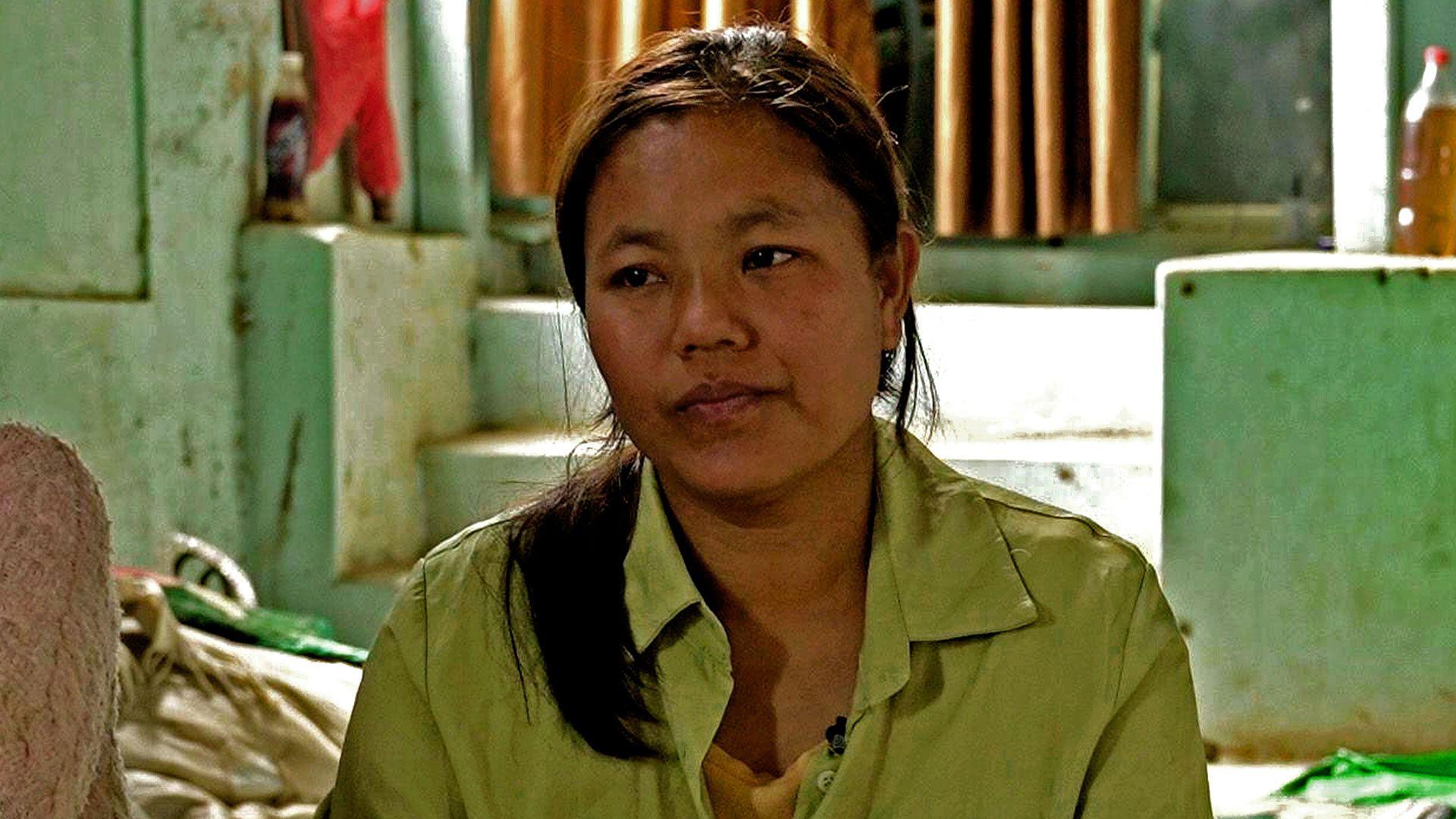 Iang Za Kim, sitting in a green shirt on the floor of a community centre in India