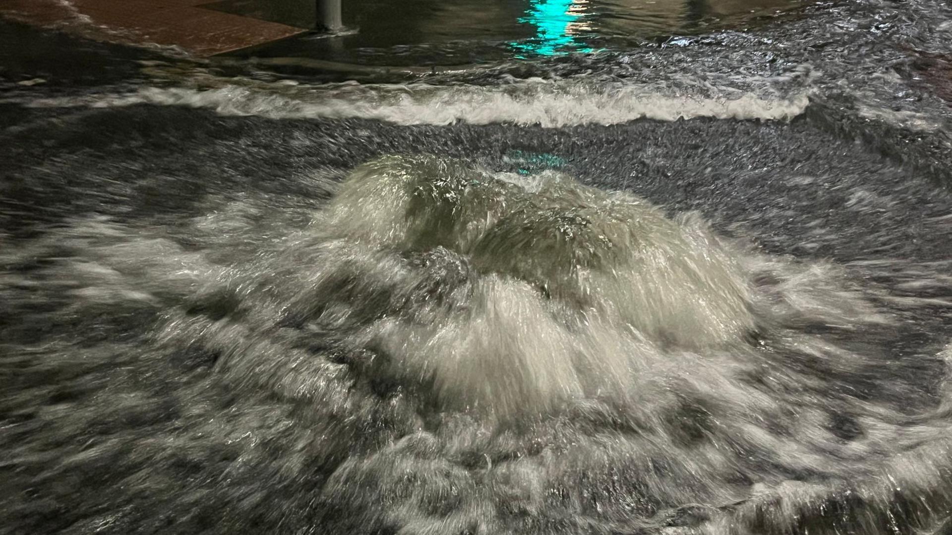 Water surges out of a manhole cover on a road.