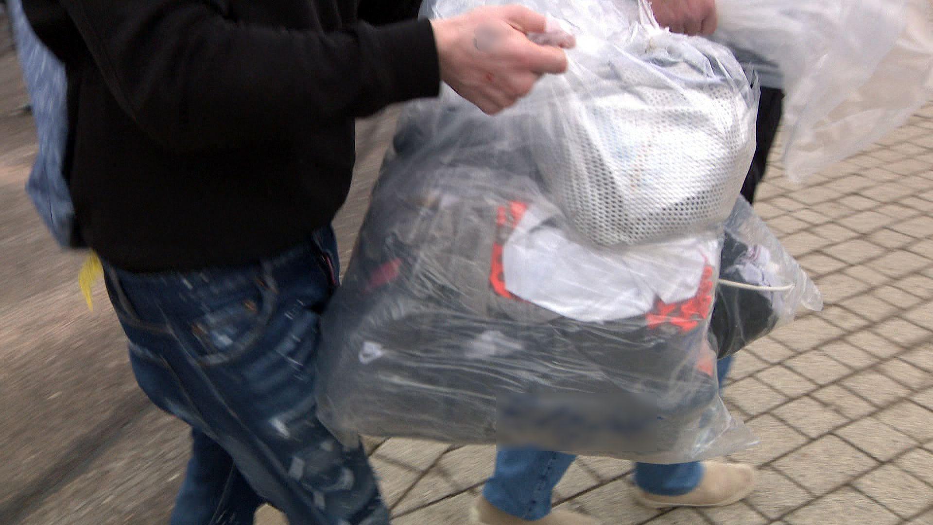 An unidentified man wearing jeans and a black jumper carries a plastic bag of belongings.