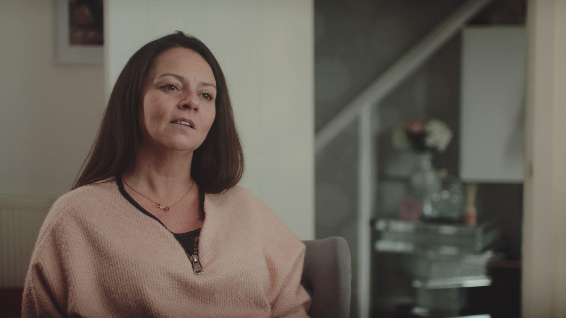 Wendy Stewart sitting inside a house with light coloured walls. She has shoulder-length brown hair and is wearing a beige top.
