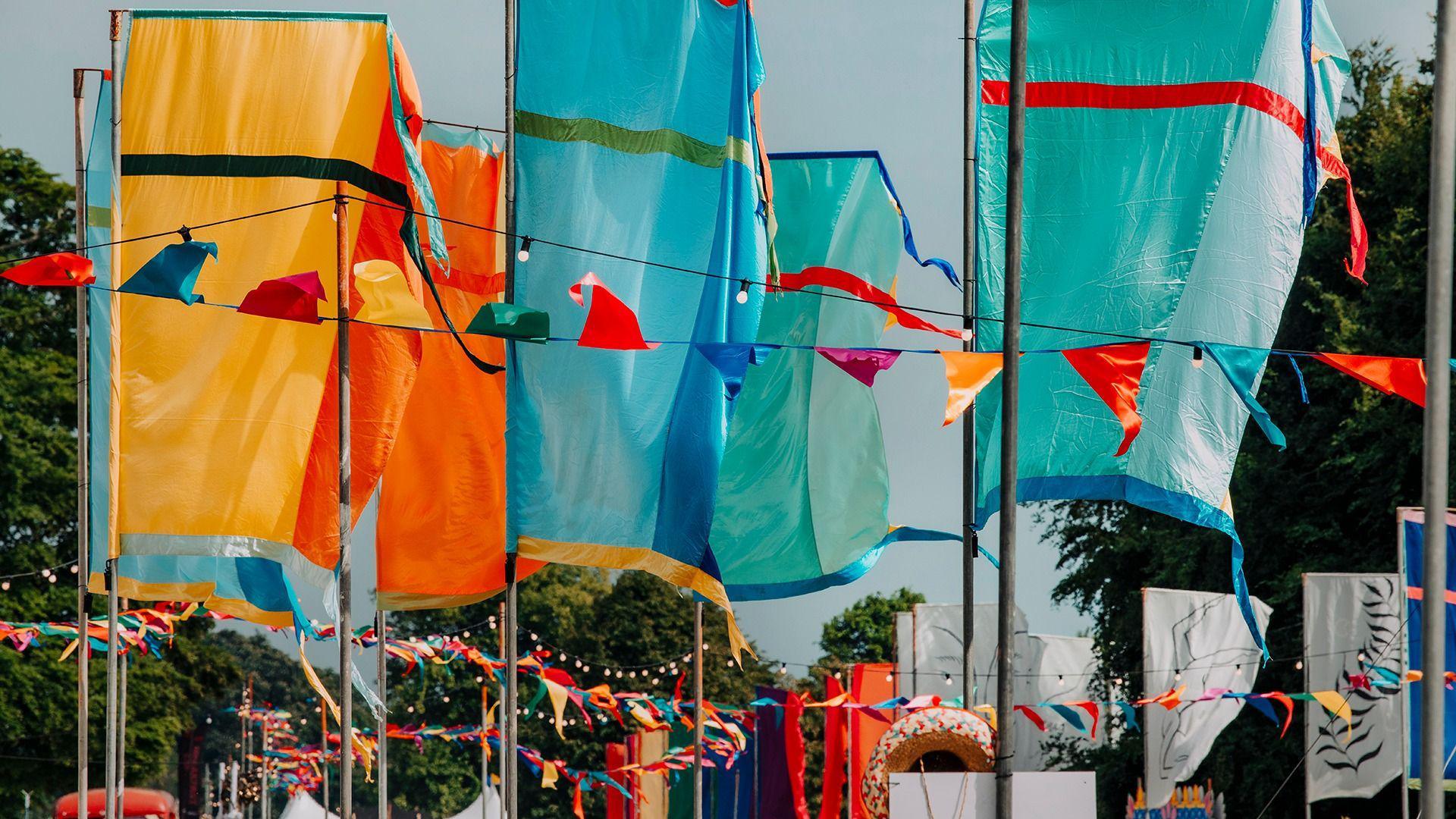 Bridge yellow and blue festival flags with ribbons in similar colours fluttering underneath. The festival is based among green trees.