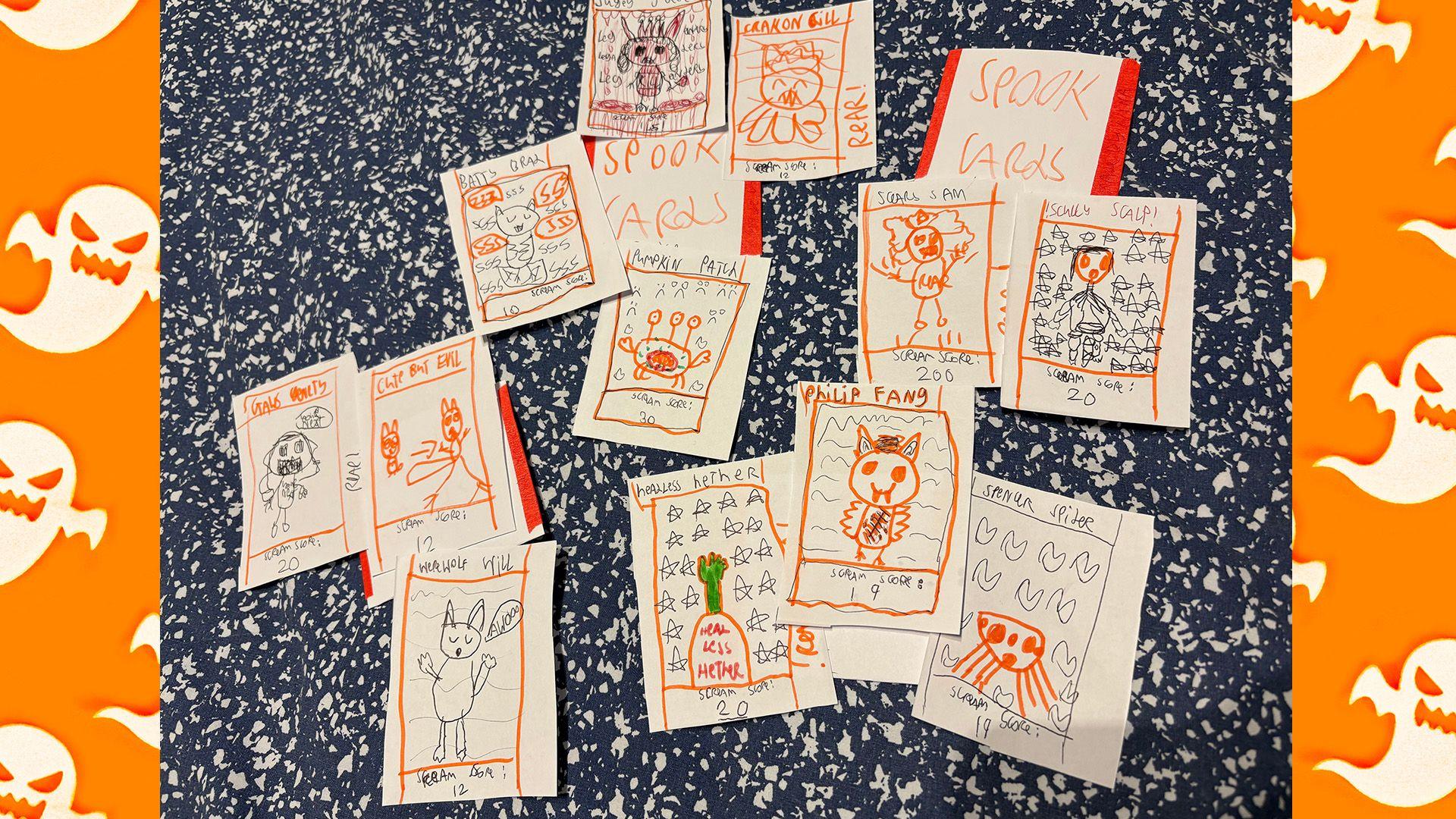 Around 15 cards sit on a table spread out. They have hand drawn characters on them like cats and spiders. Some say spook cards on them