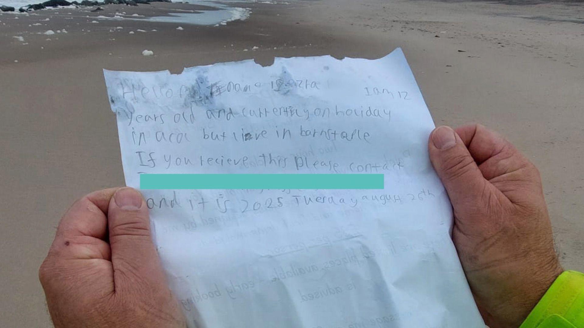 The piece of paper reads: "Hello, my name is Ezra I am 12 years old and currently on holiday in Alcol but live in Barnstaple. If you receive this please contact (redacted) and it is 2025 Tuesday August 26th".