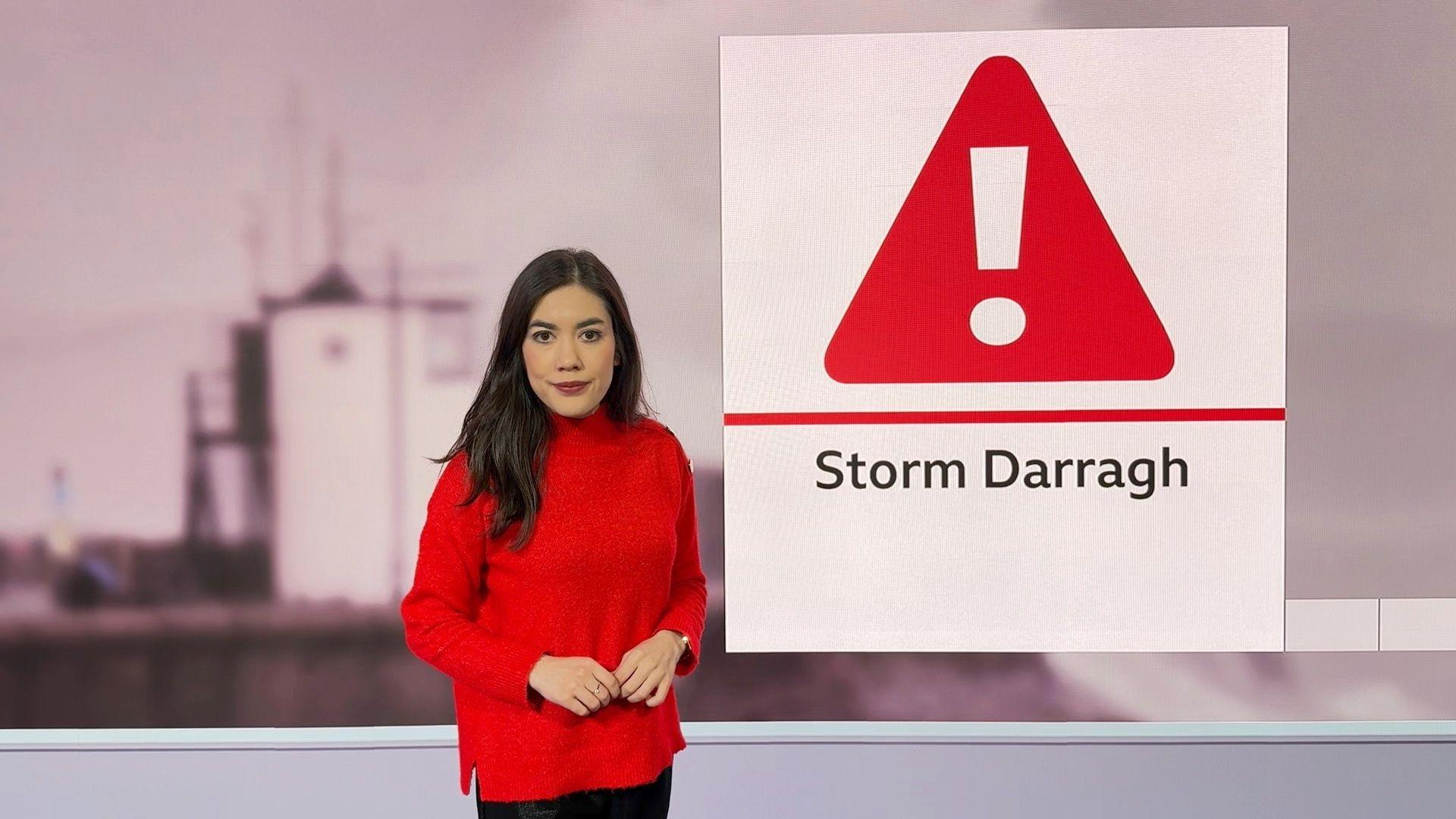 Sabrina in a red jumper looking at he camera. Next to her is a red warning sign, and underneath it says Storm Darragh