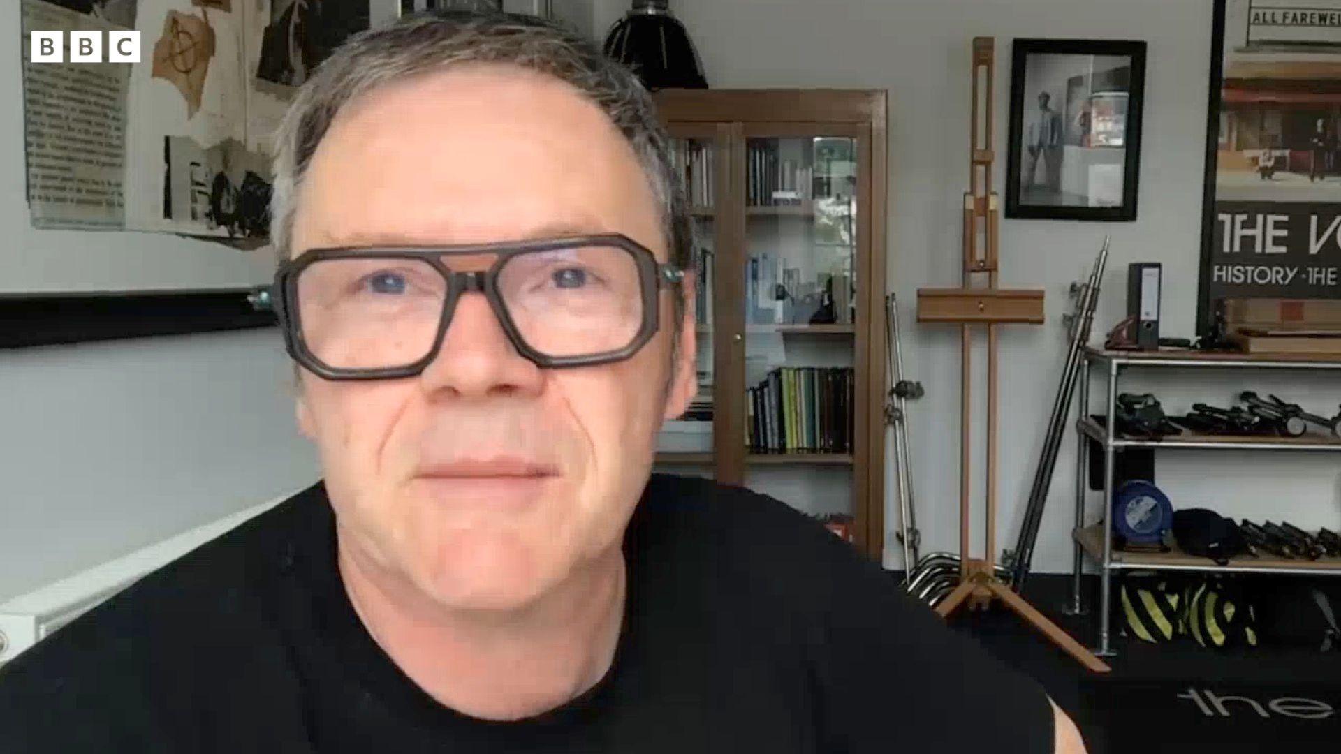 Brian Cannon, who is wearing a black t-shirt and black, square-rimmed glasses, sits in his studio on a Zoom call to the BBC