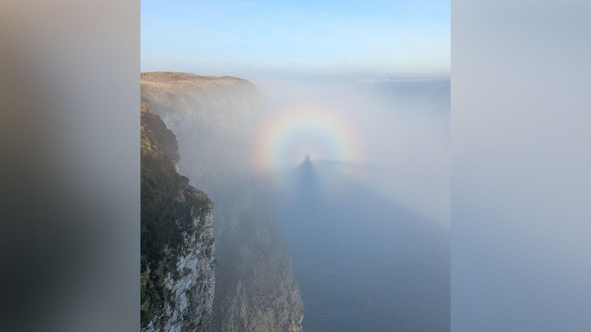 An image of a person's shadow, encased in a rainbow, off Bempton Cliffs in East Yorkshire. It is a sunny day with a fret coming from the sea