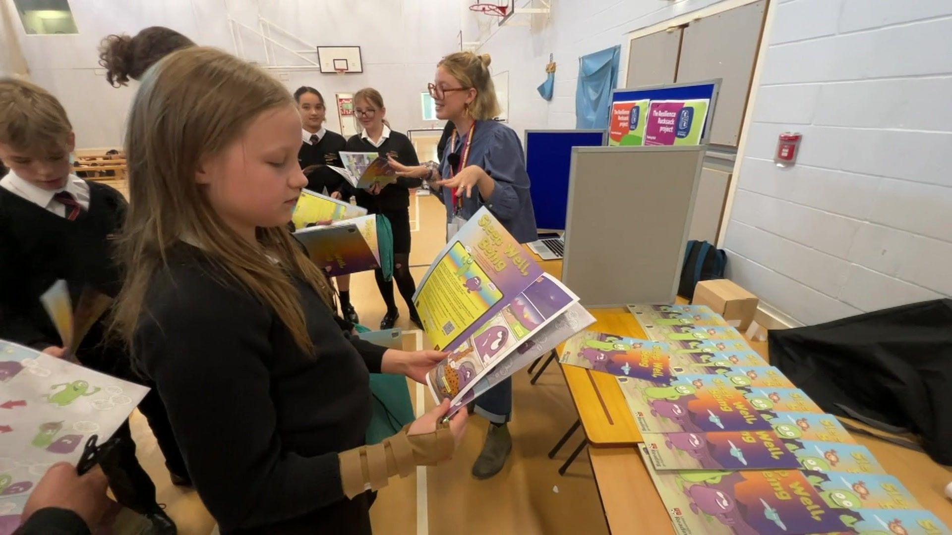 A school pupil who is stood in the school hall reading a comic book on mental health and sleep