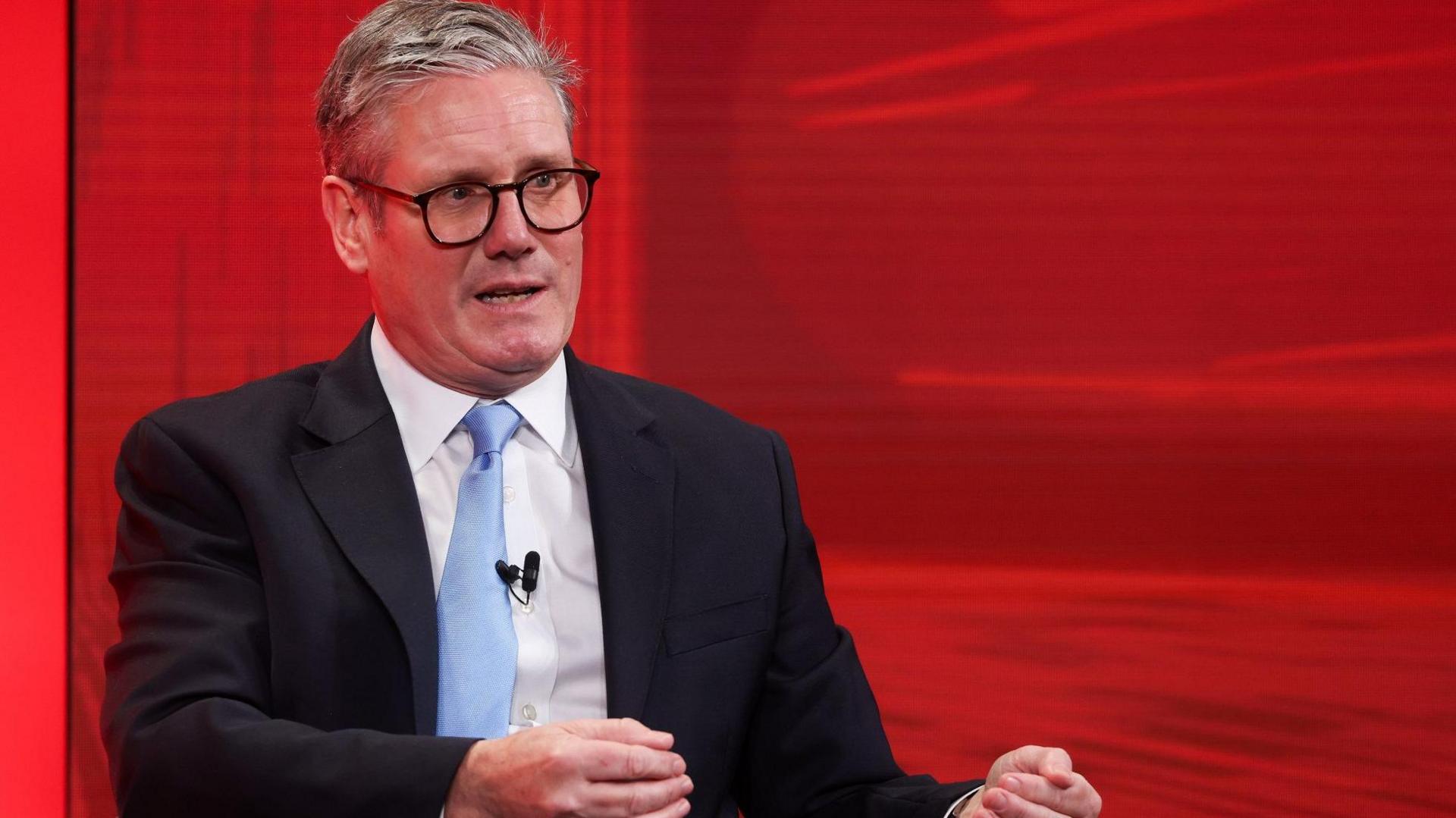 Sir Keir Starmer speaking at the International Investment Summit in front of a red background