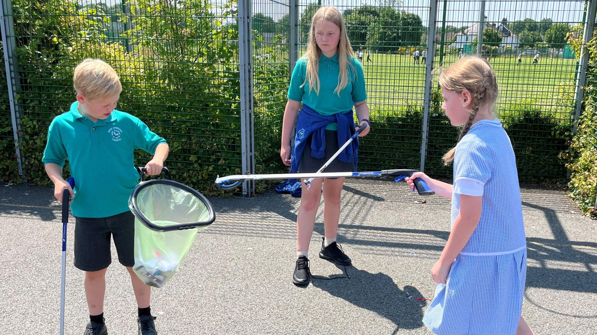 Llun o blant Ysgol Gymraeg Caerffili yn casglu sbwriel ar y iard ar ddiwrnod braf