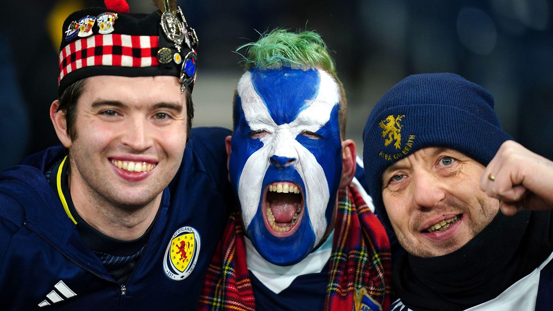 Three Scotland fans smiling and shouting wearing traditional Scotland hats and Scottish flag facepaint cheer before the match on Tuesday in Glasgow