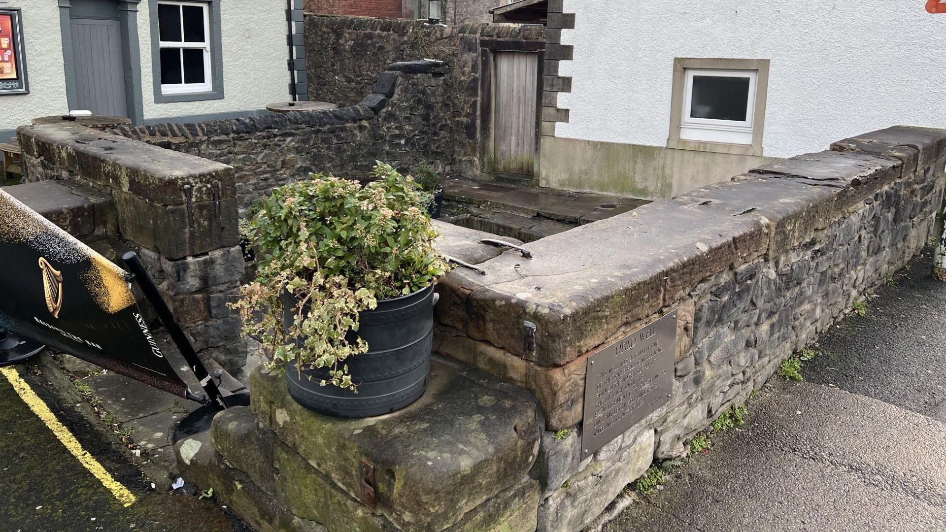 A stone well made up of two brick walls attached to a white building