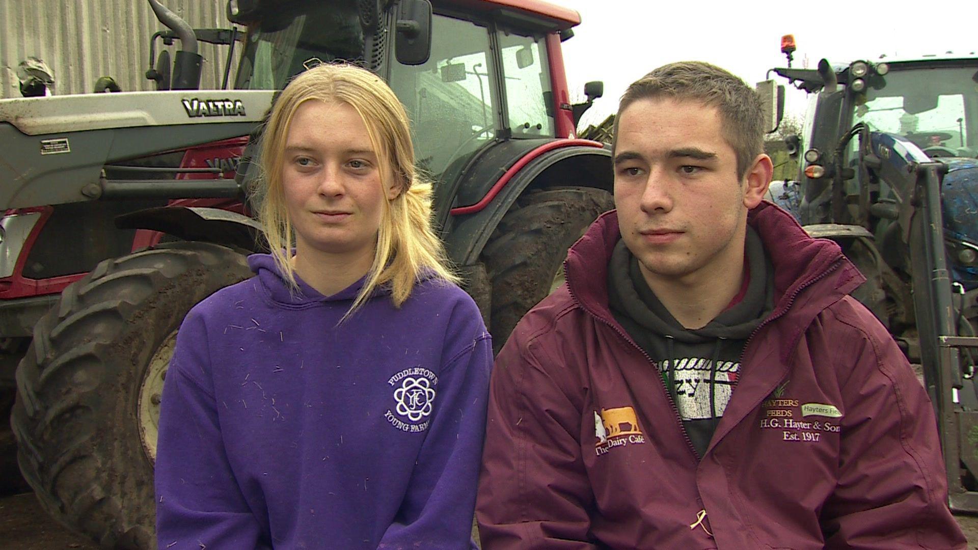 Tristan Hayter and Rowena Jones from Puddletown Young Farmers in Dorset giving an interview. They are looking away from the camera. There are tractors behind them.