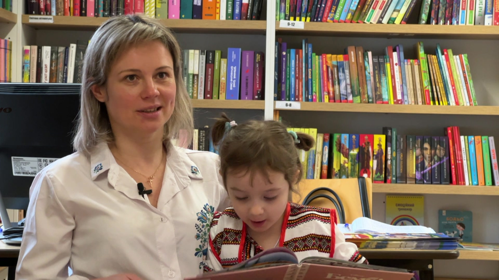 Oksana looking at the camera as Diana reads a children's book.