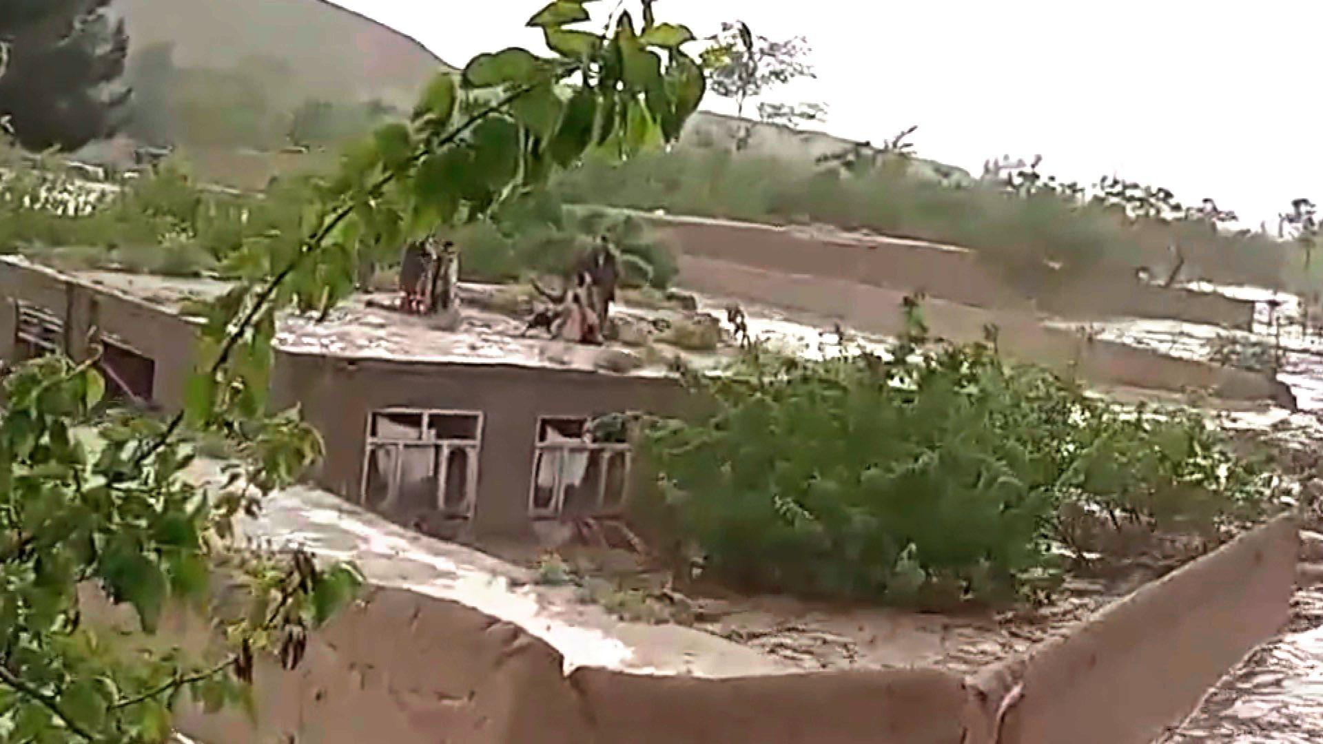 A still from a video shows people perching on the roof of a building encompassed by flood water