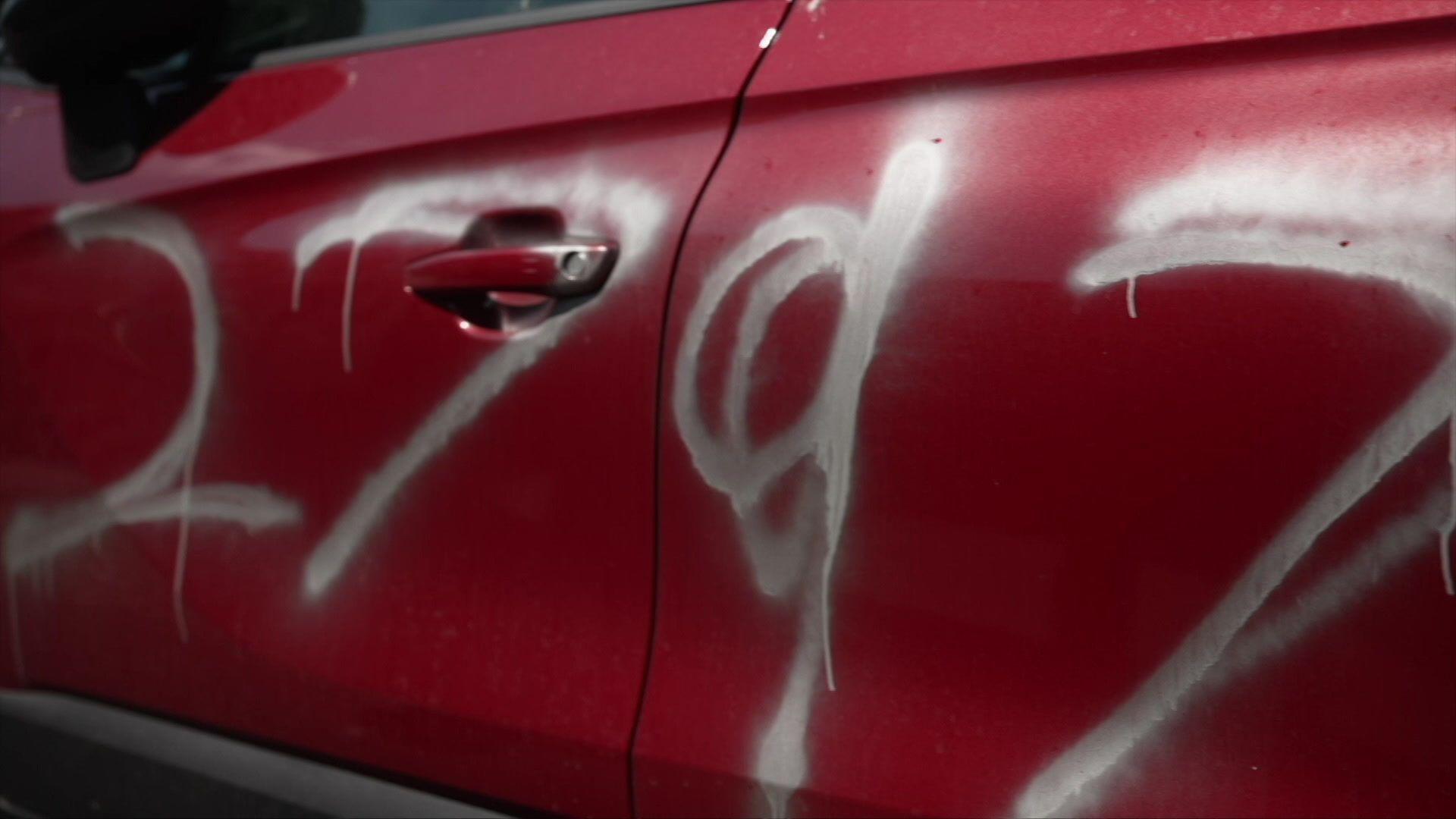 Sandra's red car can be seen with white graffiti on the door