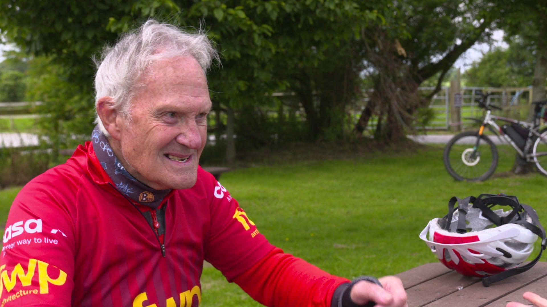 Tony Newton sitting down in a park with his cycling clothes on and helmet and bike by the side of him