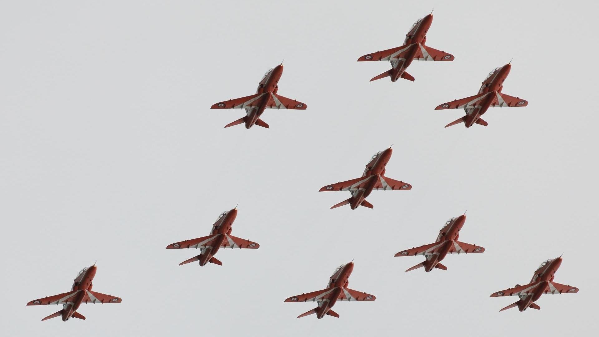The Red Arrows flying in formation, with a grey sky above them.