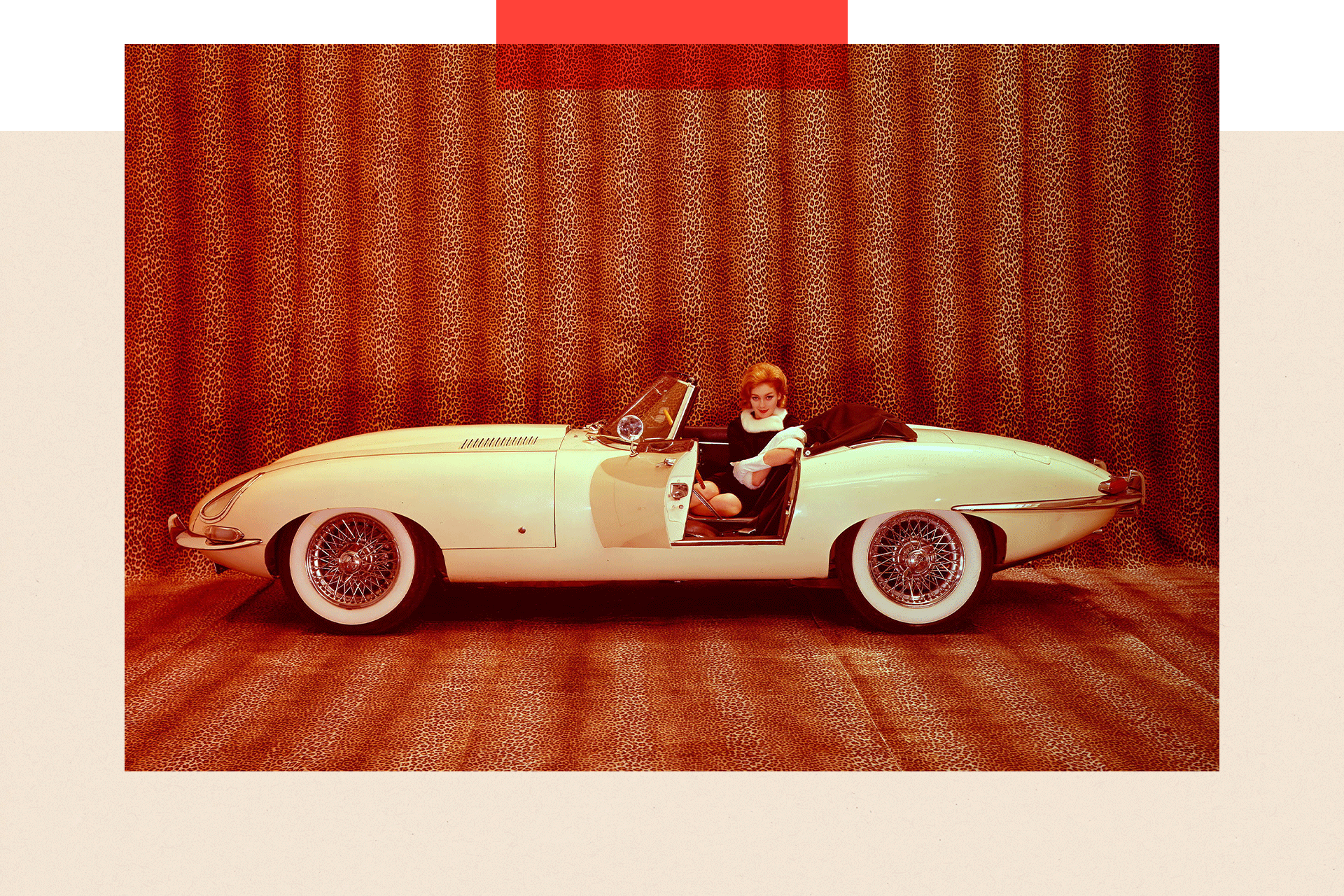 A woman poses inside a Jaguar E-Type Series I OTS with its left door open