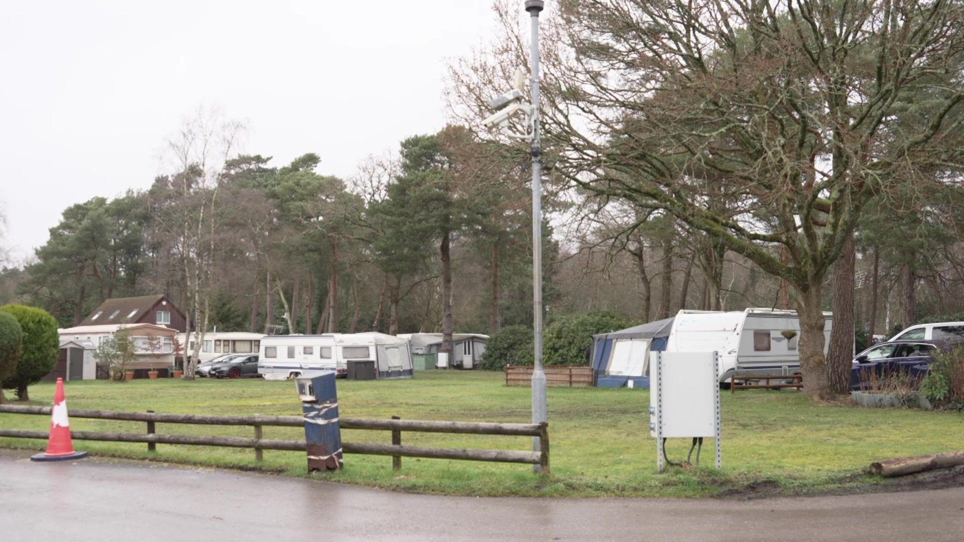 A row of caravans in a field with a line of trees behind them. It's an overcast day.