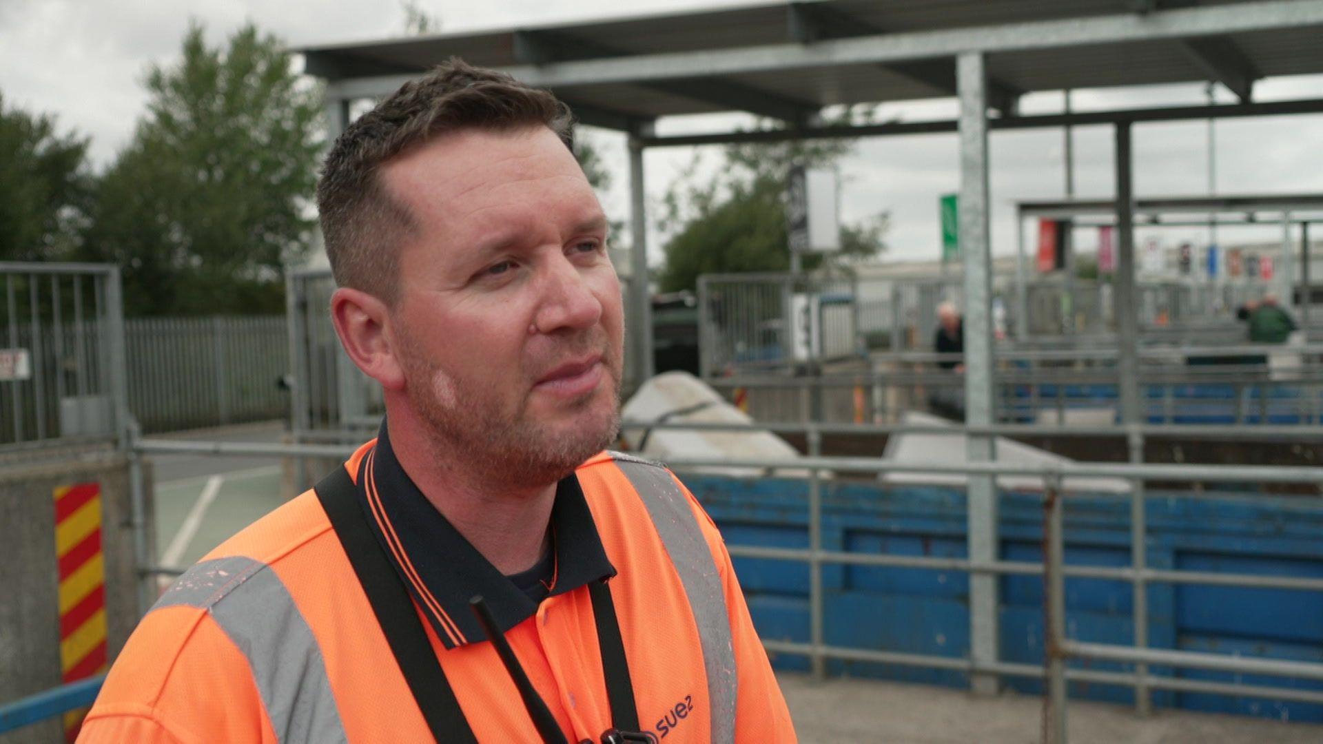 Michael Peers, a waste worker, stands on site wearing an orange high-viz polo shirt