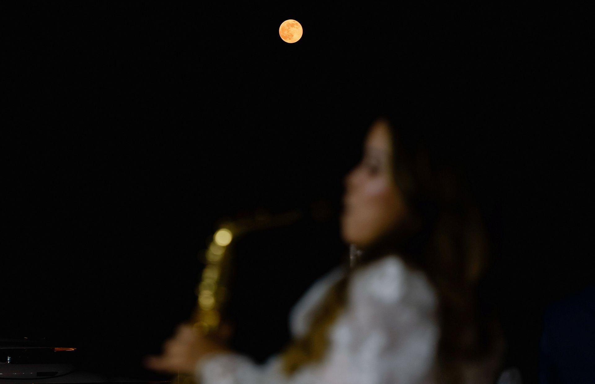 The female musician can be seen in the foreground but out of focus, while the Moon shines very orange against a starless night sky in Doha on Wednesday.