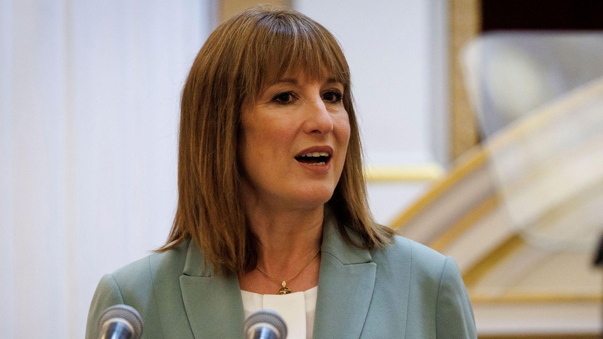 Chancellor Rachel Reeves wearing a sage green jacket and white collarless blouse stands behind a podium with two microphones giving a speech at the annual Mansion House dinner in the City of London, UK.