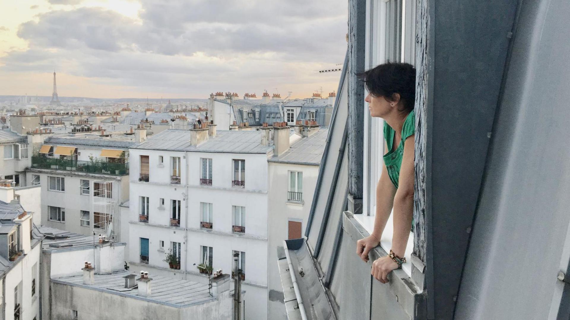 Kate leans out of the window as she overlooks the city's skyline. The Eiffel tower can be seen in the background on the left.