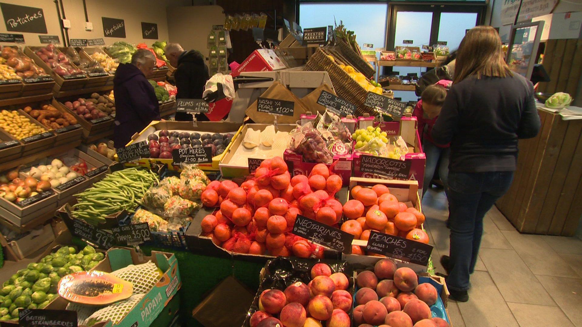 A fruit and vegetable shop, with people shopping for fresh produce.