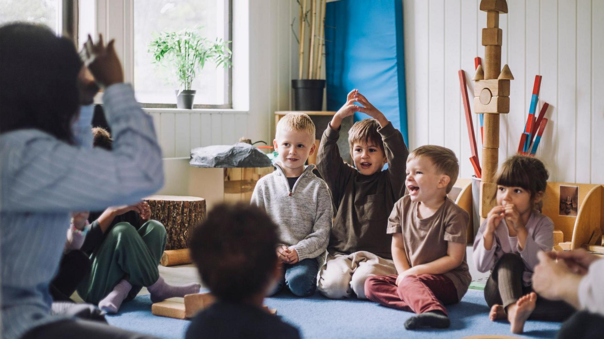 A Female child care worker wears a blue and white striped shirt, she's teaching boys and girls in day care center