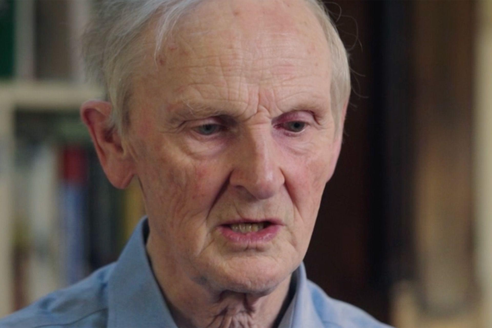 a close up of the face of a man with thin grey hair wearing a blue shirt