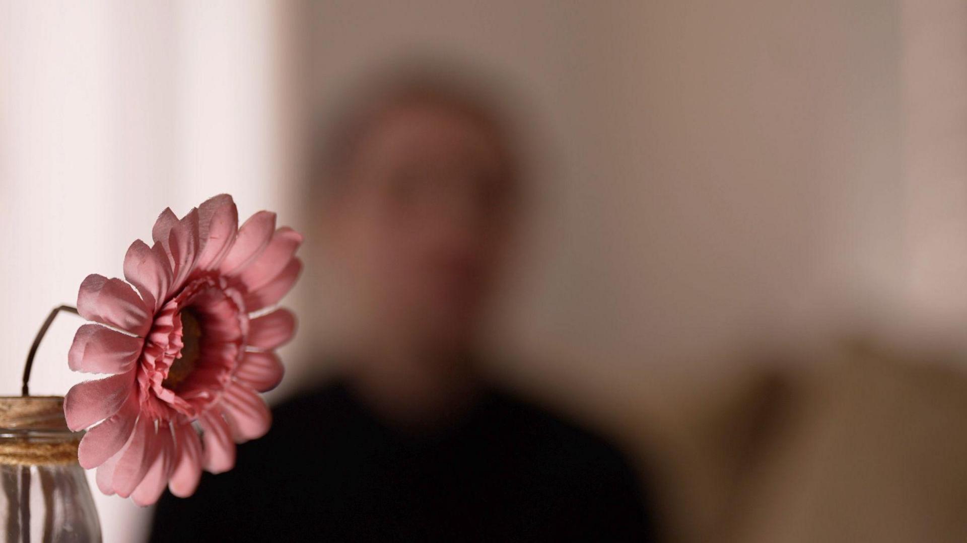 Blurred silhouette of Kate with a pink flower in the foreground.