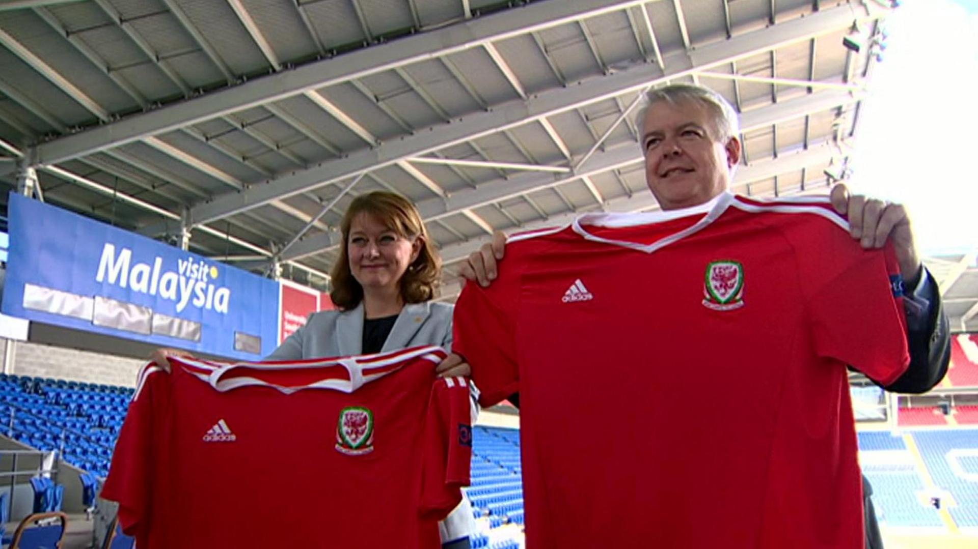 Llun o Leanne wood a Carwyn Jones gyda'i gilydd yn Stadiwm Dinas Caerdydd.  Mae'r ddau yn dal crys tîm pêl-droed Cymru