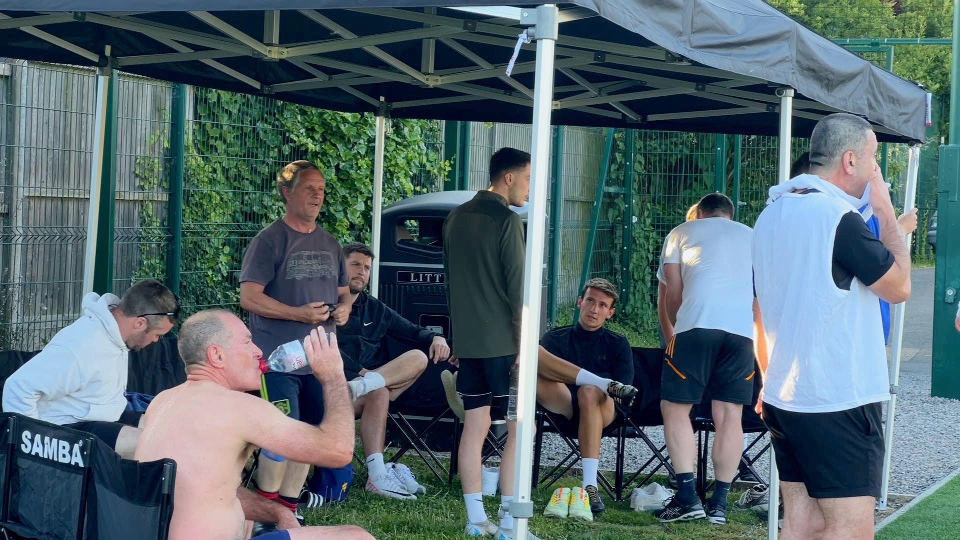 A group of men set under the marquee talking and drinking water