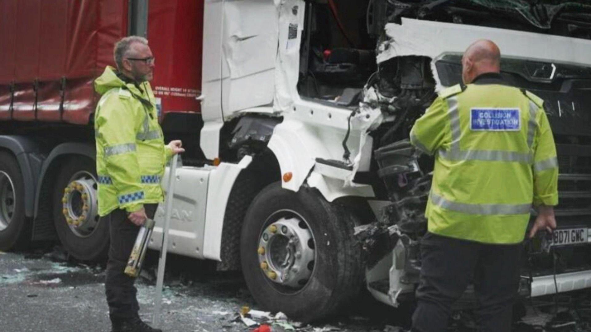 Investigators look at crashed lorries. They are both wearing hi-vis. The white and red lorry shows the impact of the crash.