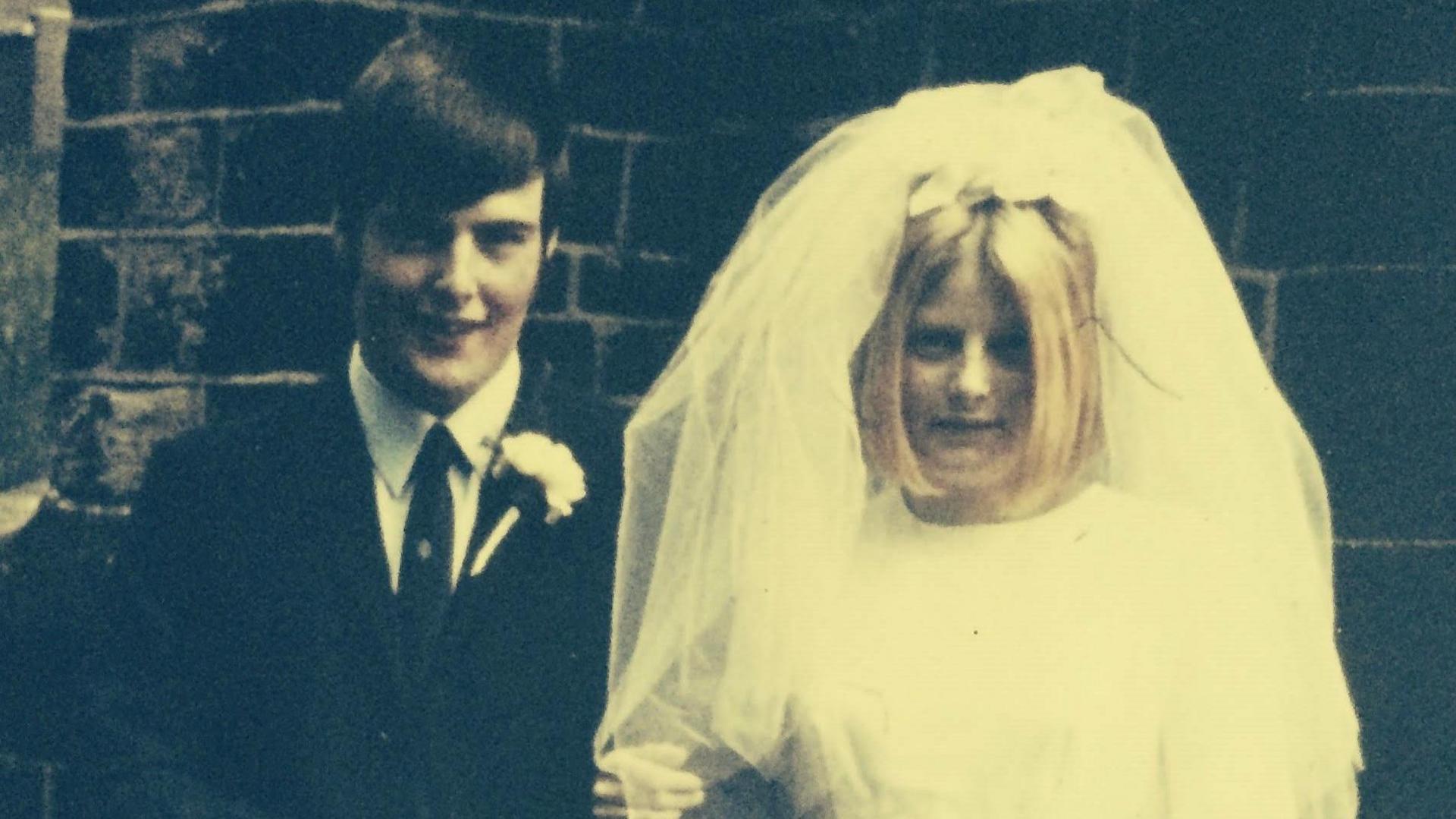 A photo of David who is on the right and Pat on the left at their wedding in 1969. David is a wearing a black suit while Pat is wearing a white wedding dress with a veil on her head.