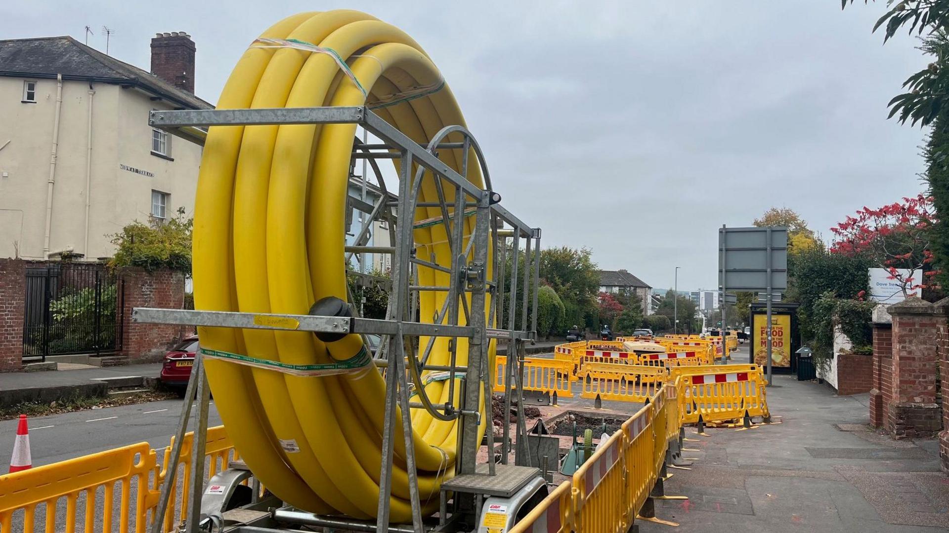 A large coil of yellow plastic piping for gas works on Heavitree Road in Exeter with yellow plastic barriers placed around it.