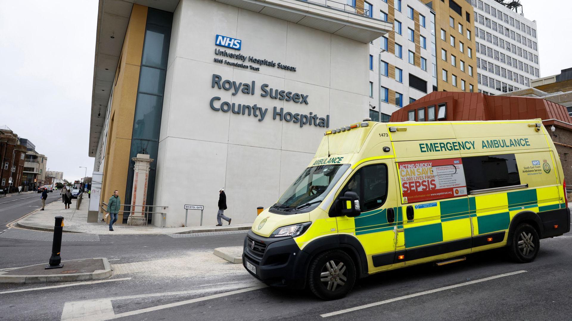 An ambulance drives past the Royal Sussex Hospital in Brighton. It is a modern building with the name of the hospital on the side in large letters.