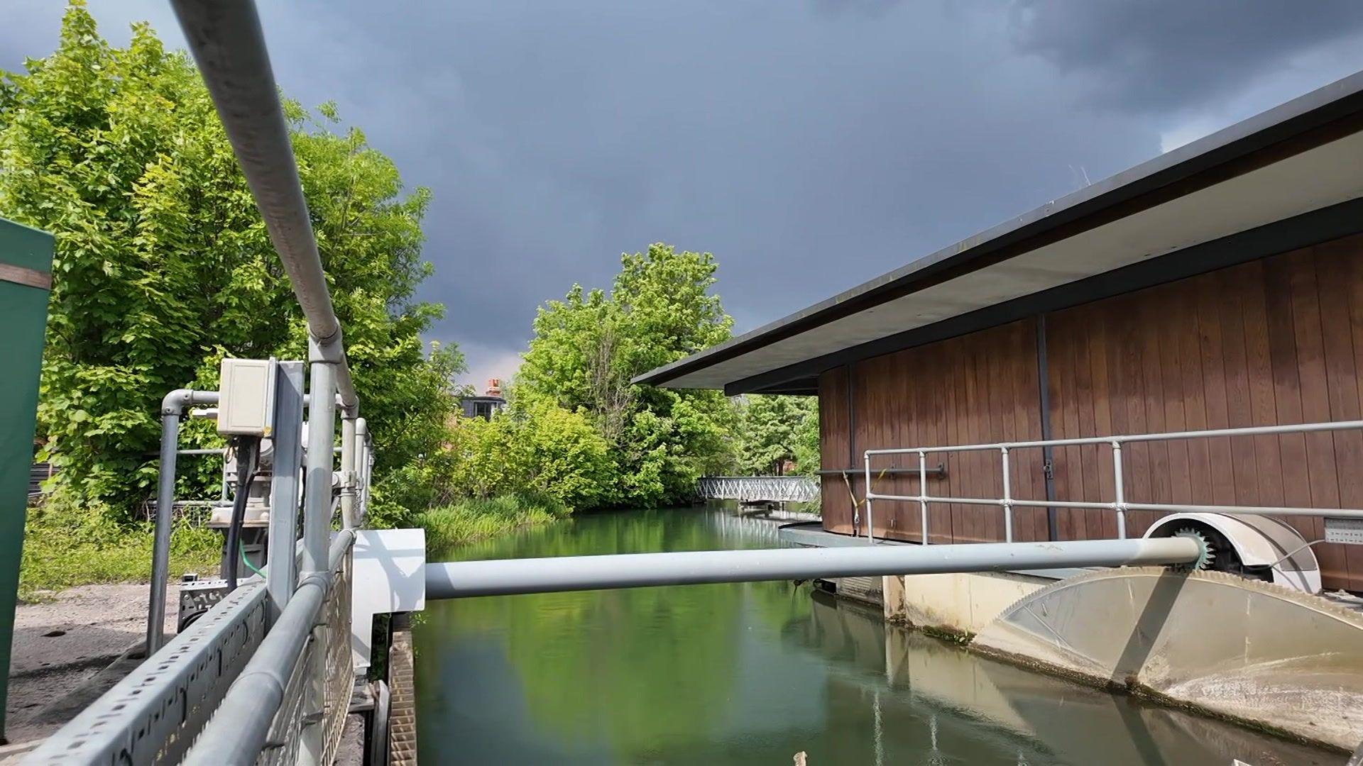 Osney Lock Hydro has a body of water running through, with mechanical equipment on one side and a wooden building on the other.