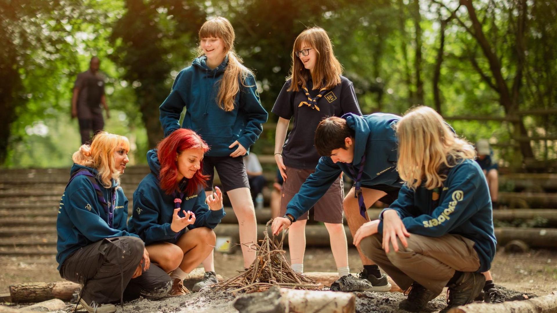 A group of Explorer scouts making a camp fire in a wooded clearning