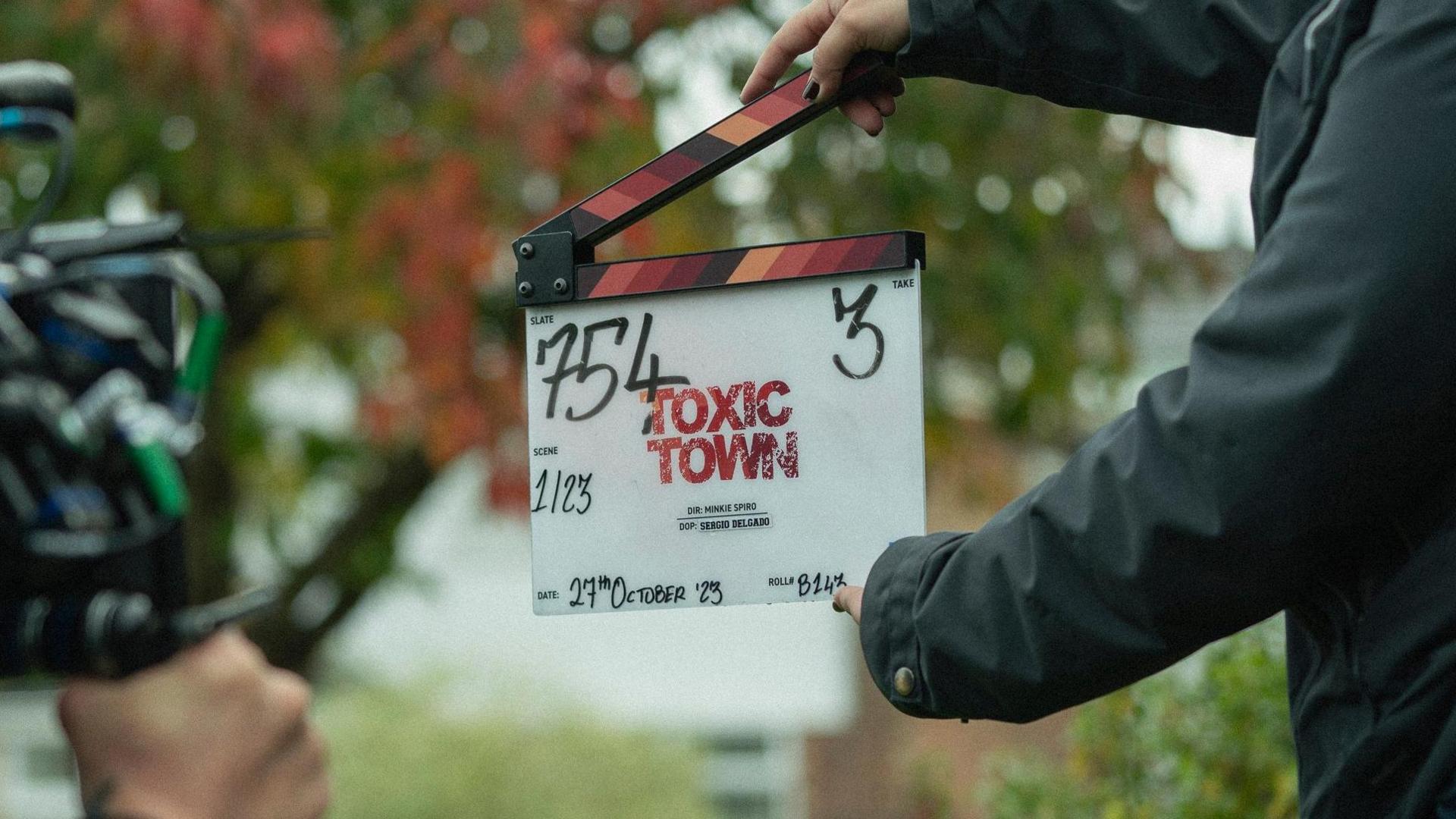 A clapperboard with the words "Toxic Town" written in large red font is being held in front of a camera on set.