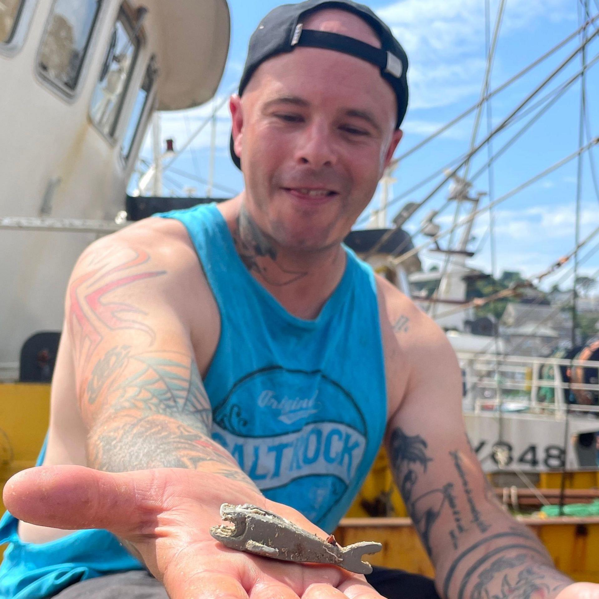 Richard West on the fishing trawler smiling broadly and looking at the grey Lego shark on his open hand