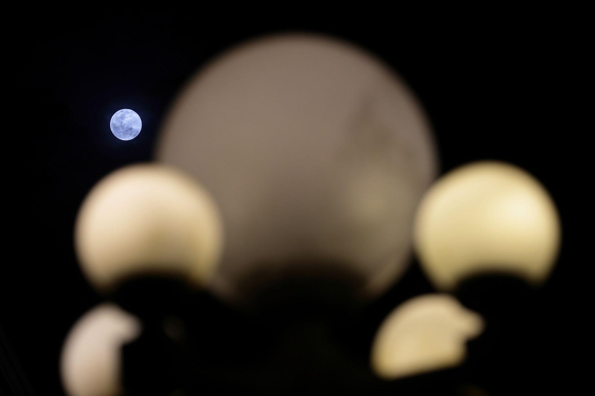 Circles of the streetlamp shine in the foreground while the Moon rises against a dark night sky in Singapore on Wednesday.