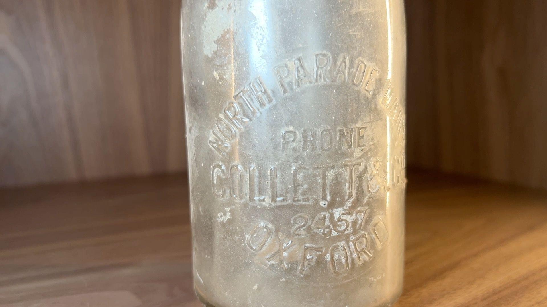 An old milk bottle on a wooden shelf.