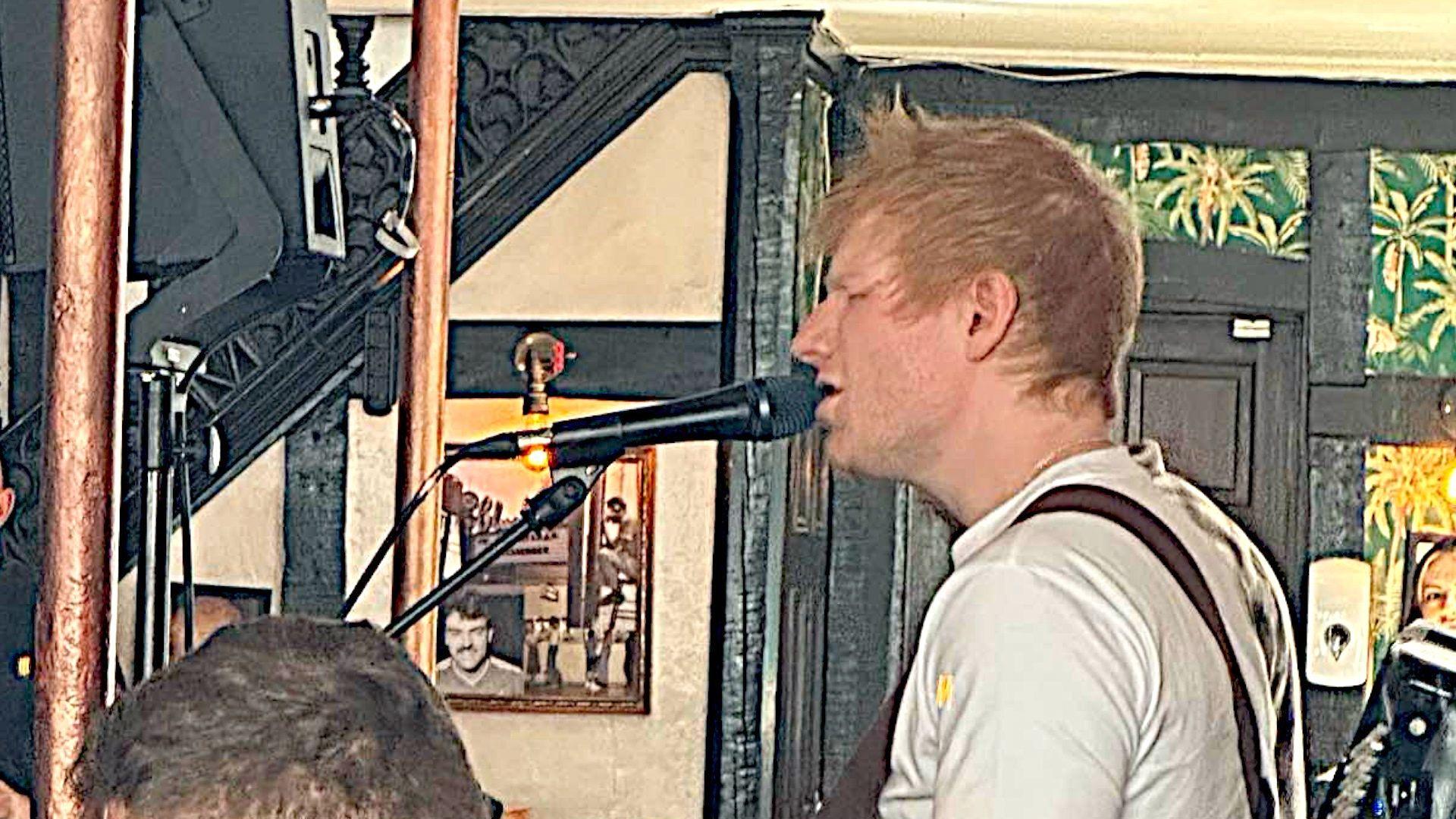 Singer Ed Sheeran at the microphone wearing a white T-shirt singing in a pub