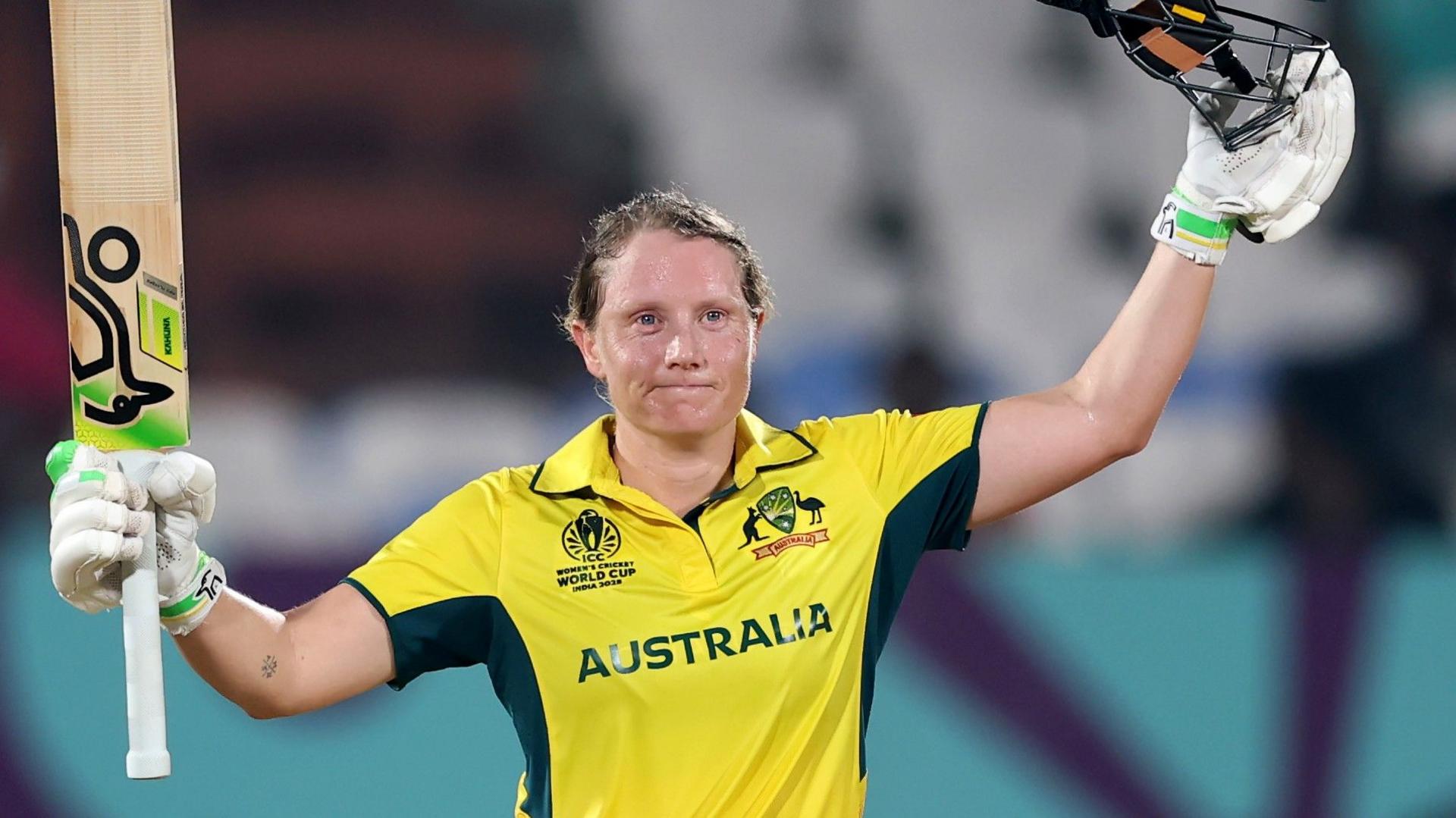 Alyssa Healy holds her bat aloft after scoring a century